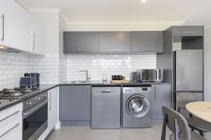 Une cuisine moderne avec des meubles gris, un lave-vaisselle encastré, un lave-linge, un four à micro-ondes et un réfrigérateur.
