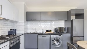 Une cuisine moderne avec des meubles gris, un lave-vaisselle encastré, un lave-linge, un four à micro-ondes et un réfrigérateur.