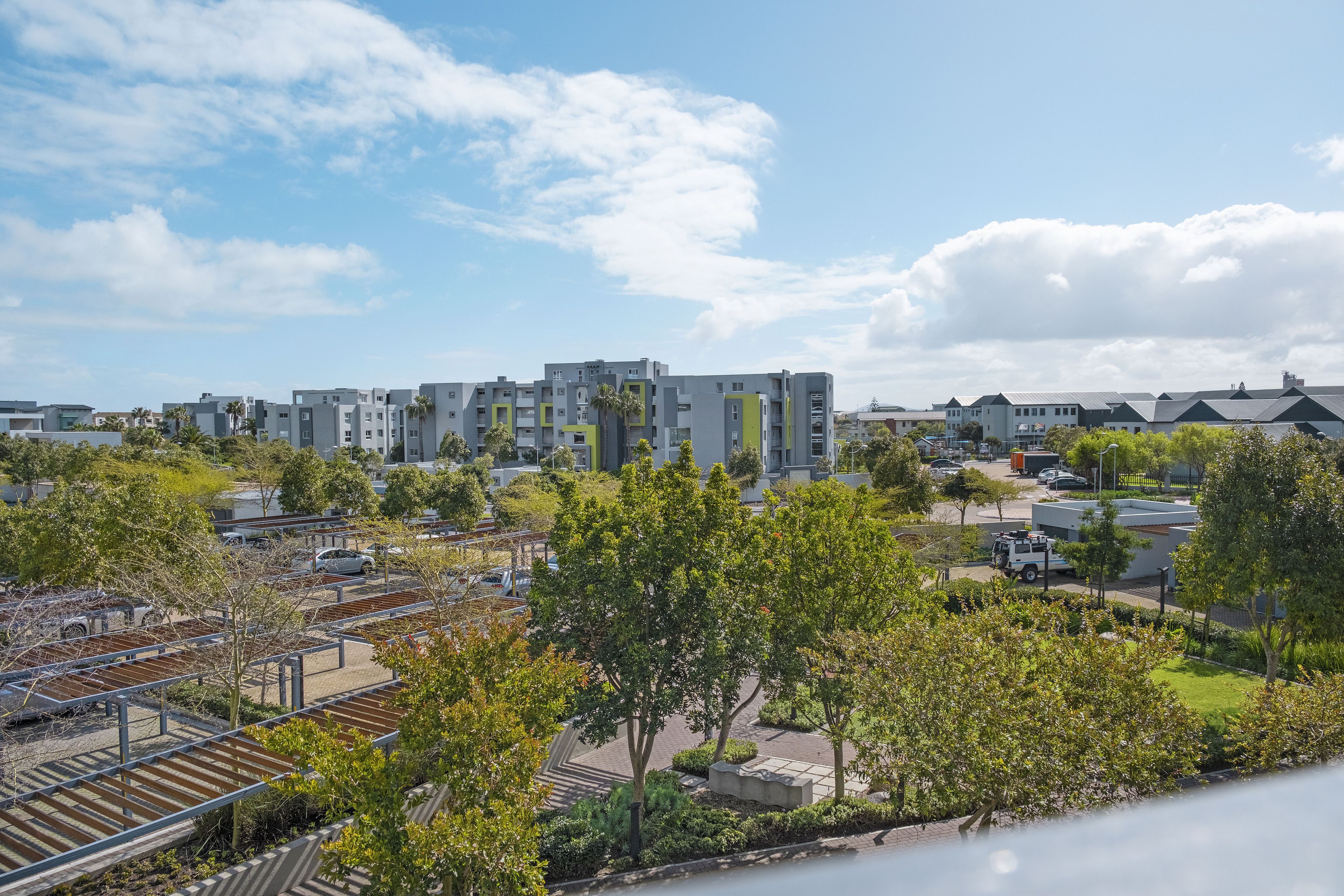 A residential area with modern apartment buildings, a parking lot, and a small park with trees.