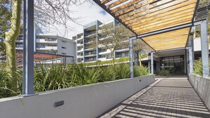 Une allée couverte avec un plafond en bois, un mur blanc agrémenté d’un jardinier, et un bâtiment avec de nombreux balcons en arrière-plan.