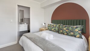 Une chambre à coucher avec un lit, une table de chevet, un miroir et une salle de bain visible à travers une porte ouverte.