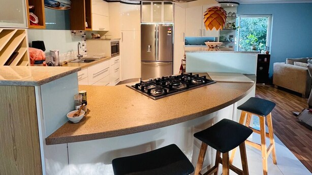 A modern kitchen with a central island, stainless steel appliances, wooden stools, and a view of the outdoors. - The Farm House
 (Possum Brush)