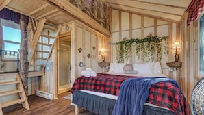 Une chambre dans une cabane en bois, avec un lit, une échelle, un bureau et une fenêtre.