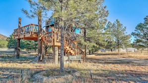 Un chalet rustique avec un escalier en bois et une terrasse, entouré de pins et surplombant un ciel dégagé.