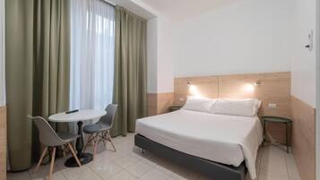 Ein Hotelzimmer mit einem Bett, einem kleinen Tisch mit zwei Stühlen und einem Fenster mit Vorhängen.