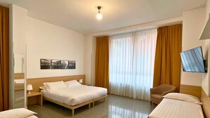 A hotel room with two single beds, a wooden headboard, a flat-screen TV mounted on the wall, a window with sheer curtains, and a small table with a lamp. - Navigli Suites (Milan)