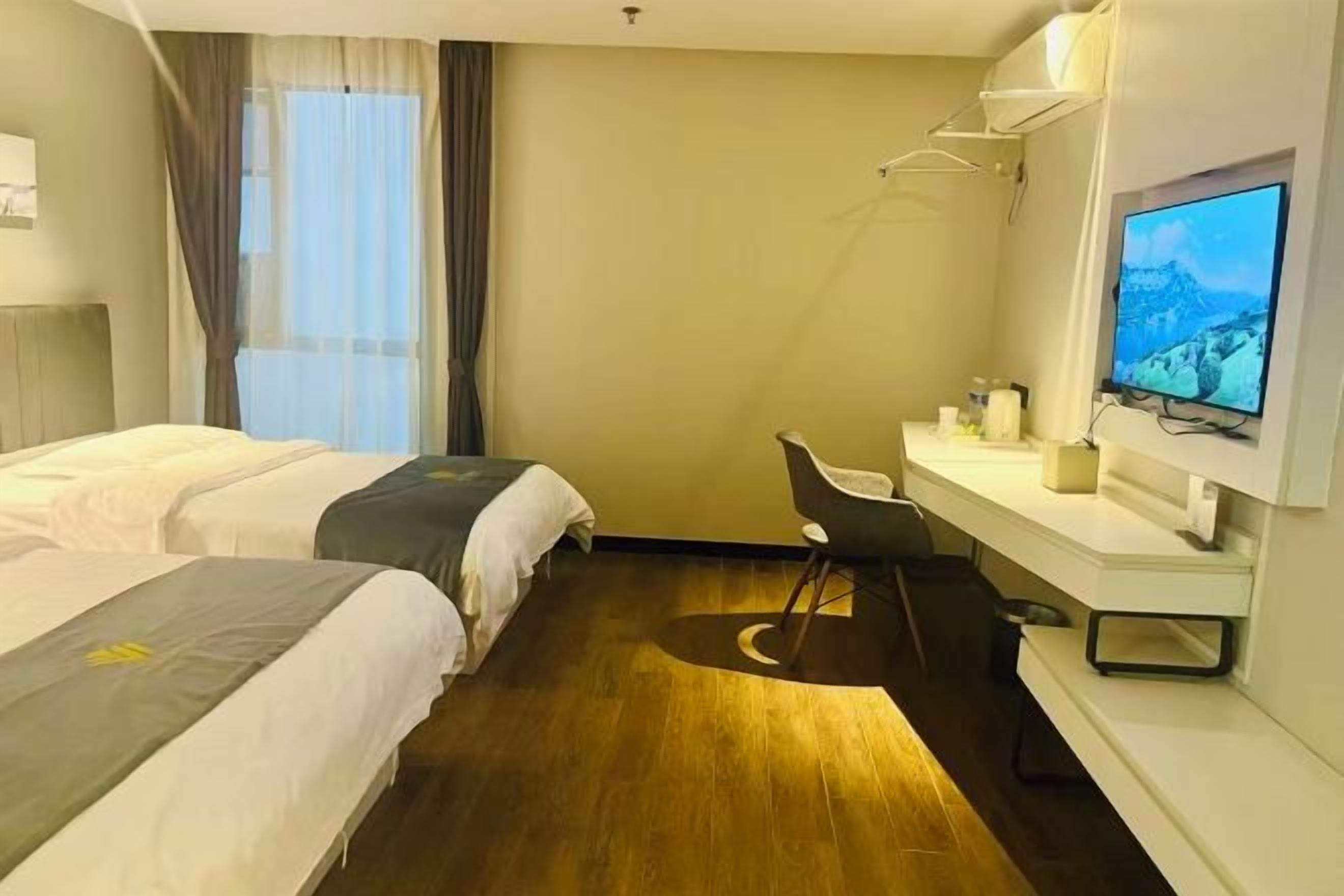 A hotel room with two beds, a desk with a chair, a television, and a window with curtains.