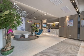 Un hall d’entrée moderne avec un comptoir d’accueil, un espace salon et une grande plante en pot.
