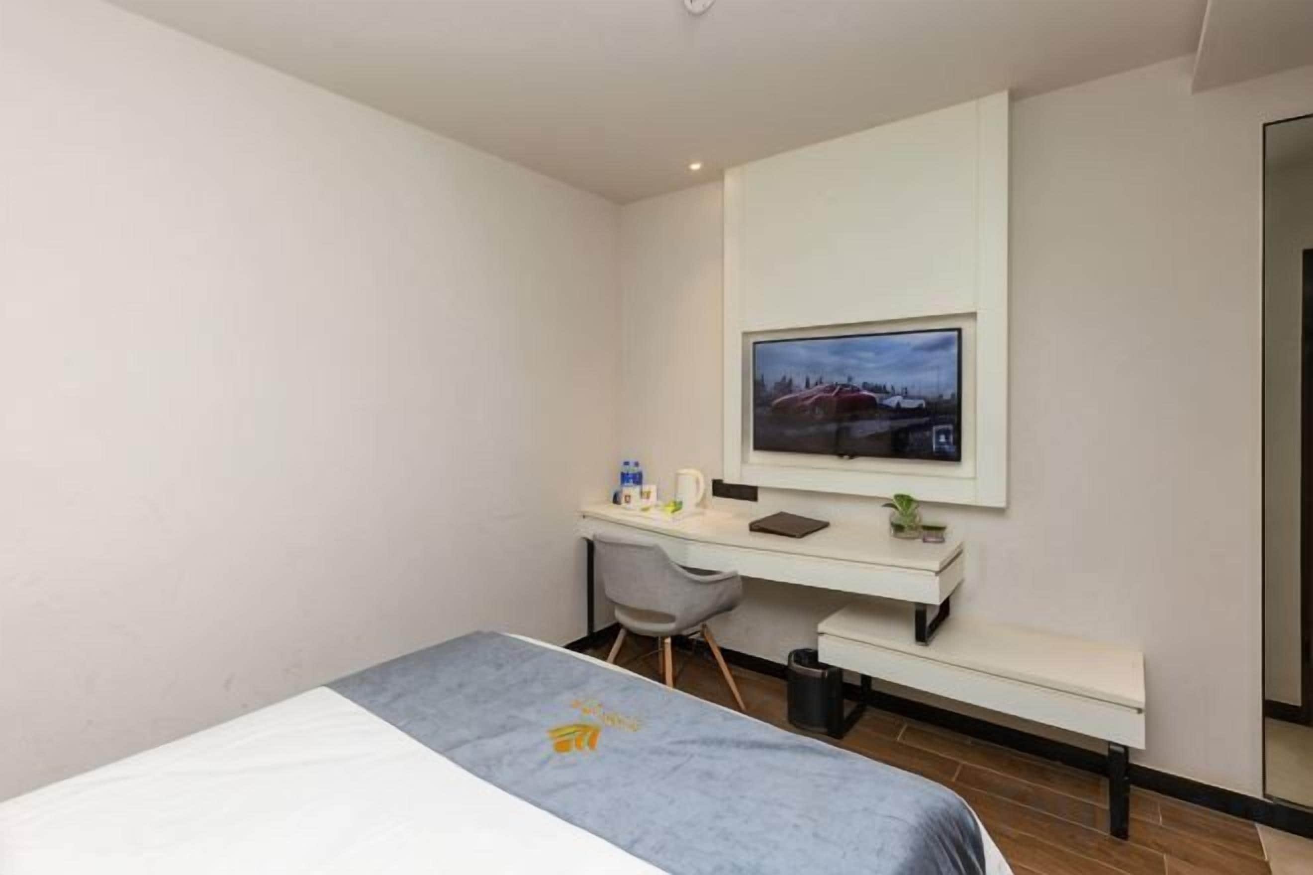 A hotel room with a bed, a desk, a chair, a television, and a small window.