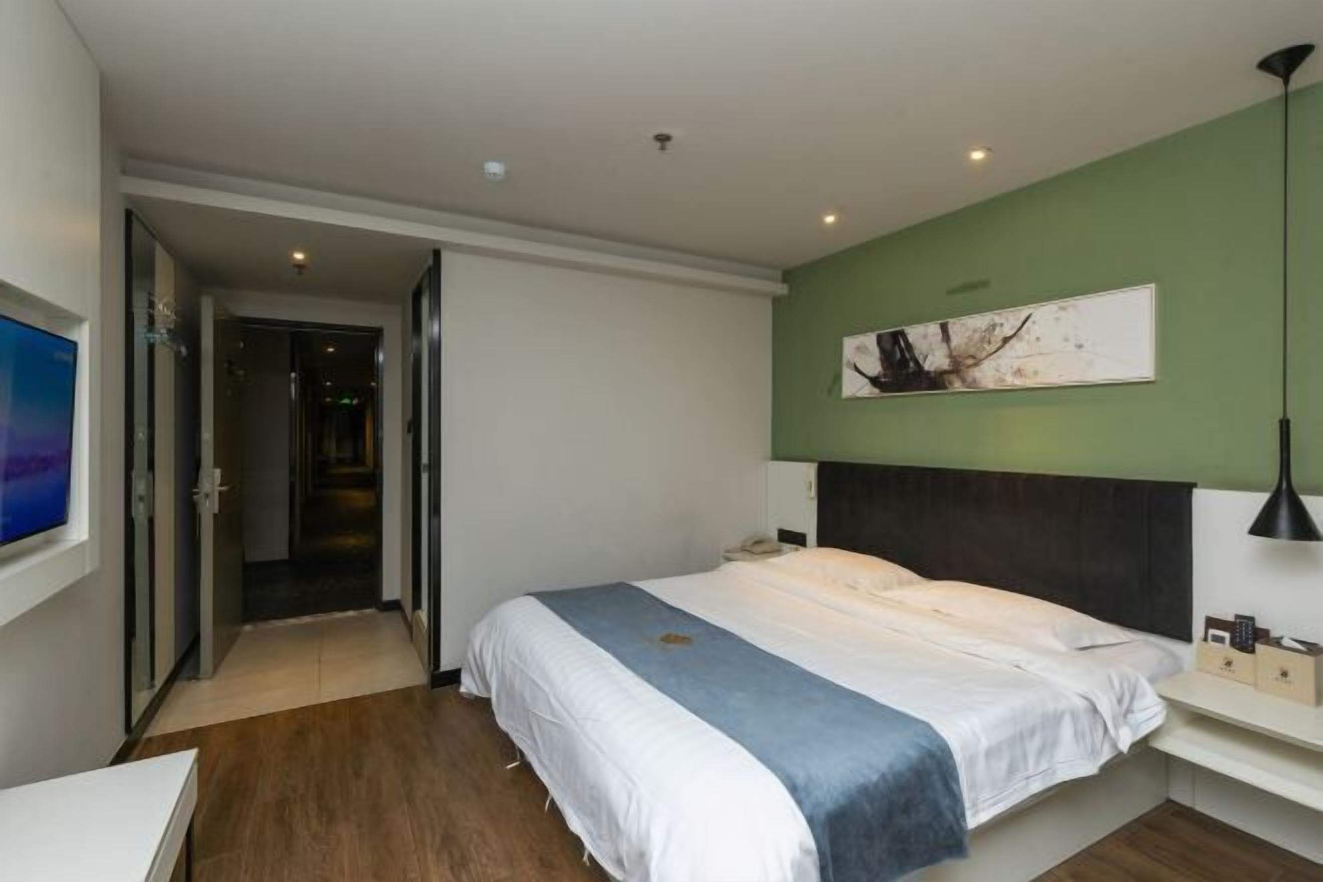 A modern hotel room with a large bed, a bedside table, a flat-screen TV, and a green accent wall.