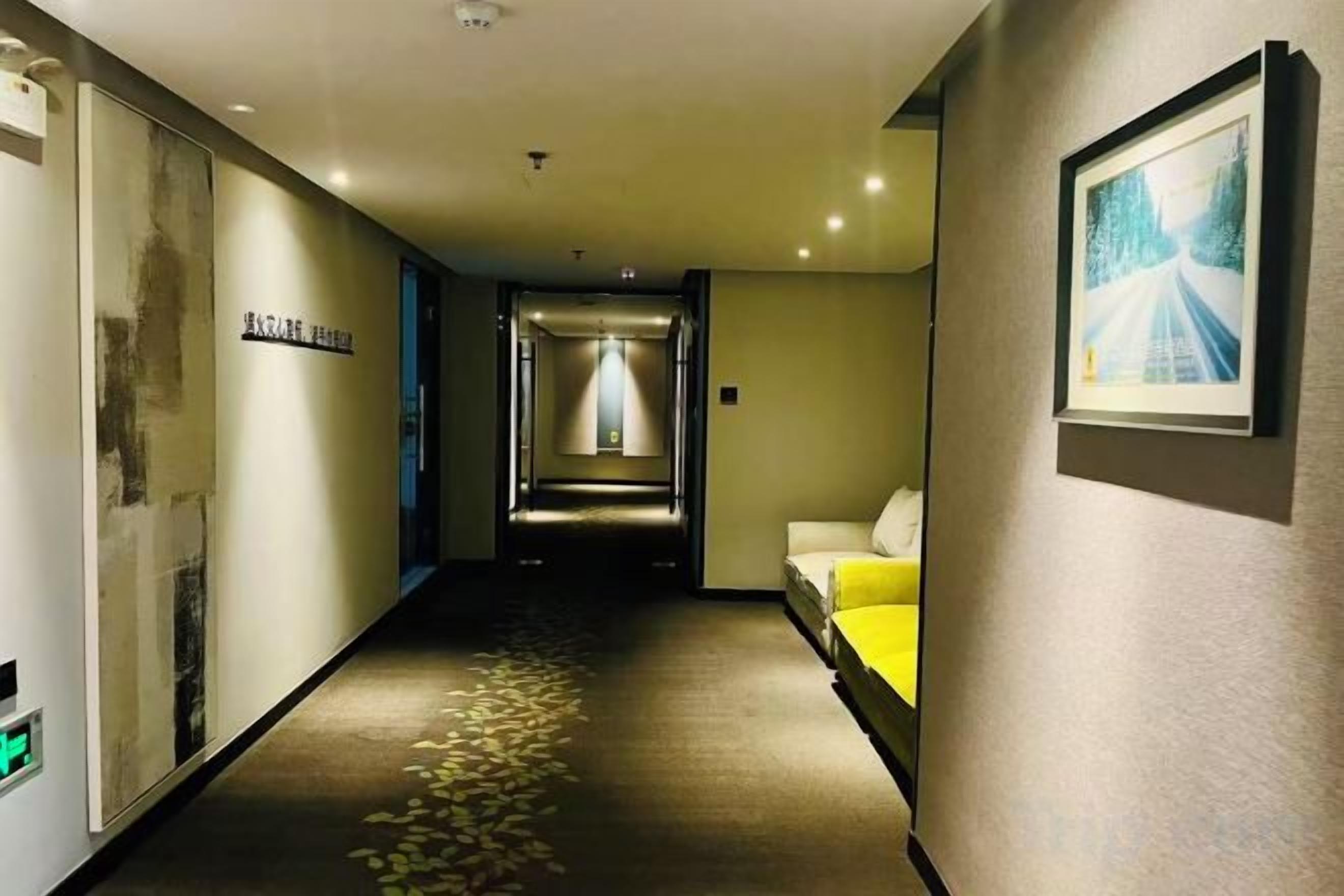 A hotel corridor with a bed, a framed picture on the wall, and a sign on the left.