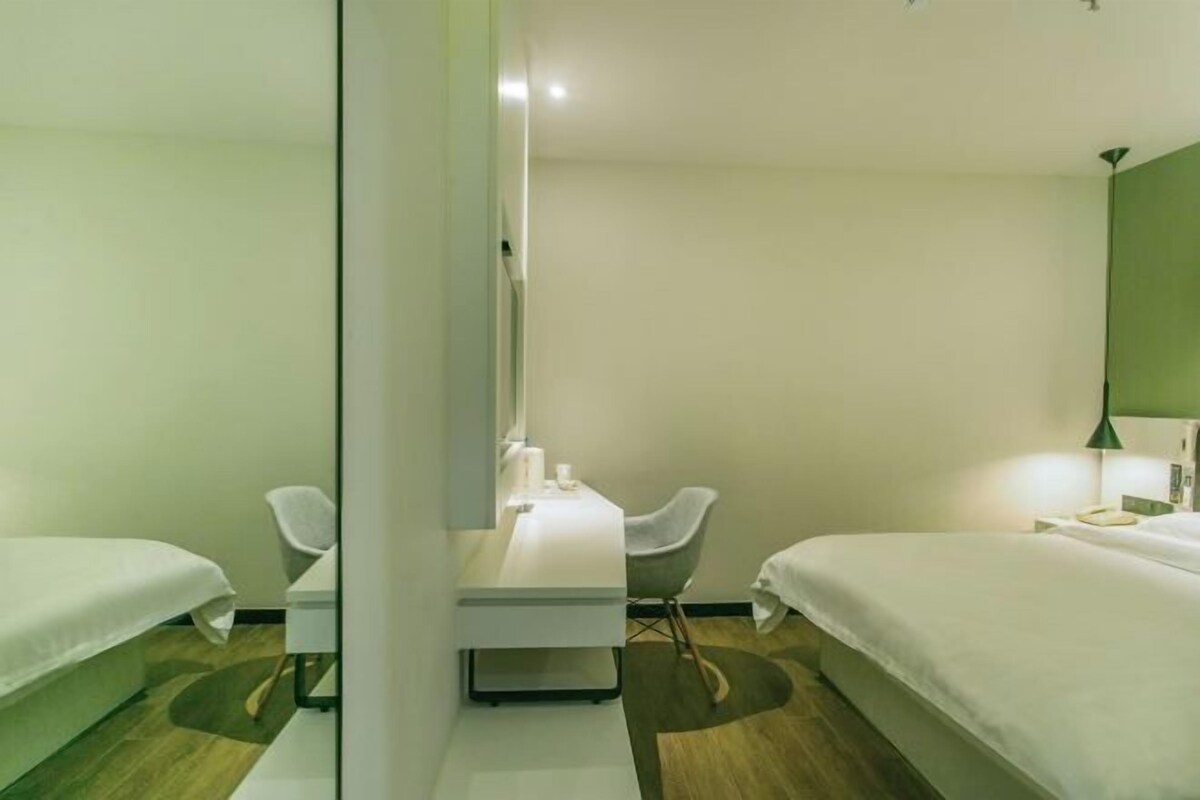 A hotel room with two beds, a desk, a chair, and a mirror.