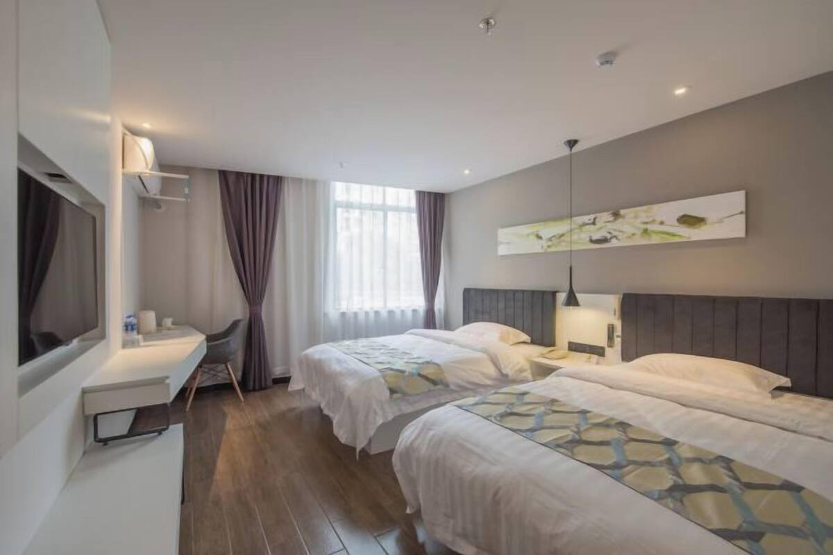A hotel room with two beds, a desk, a chair, and a large window with curtains.