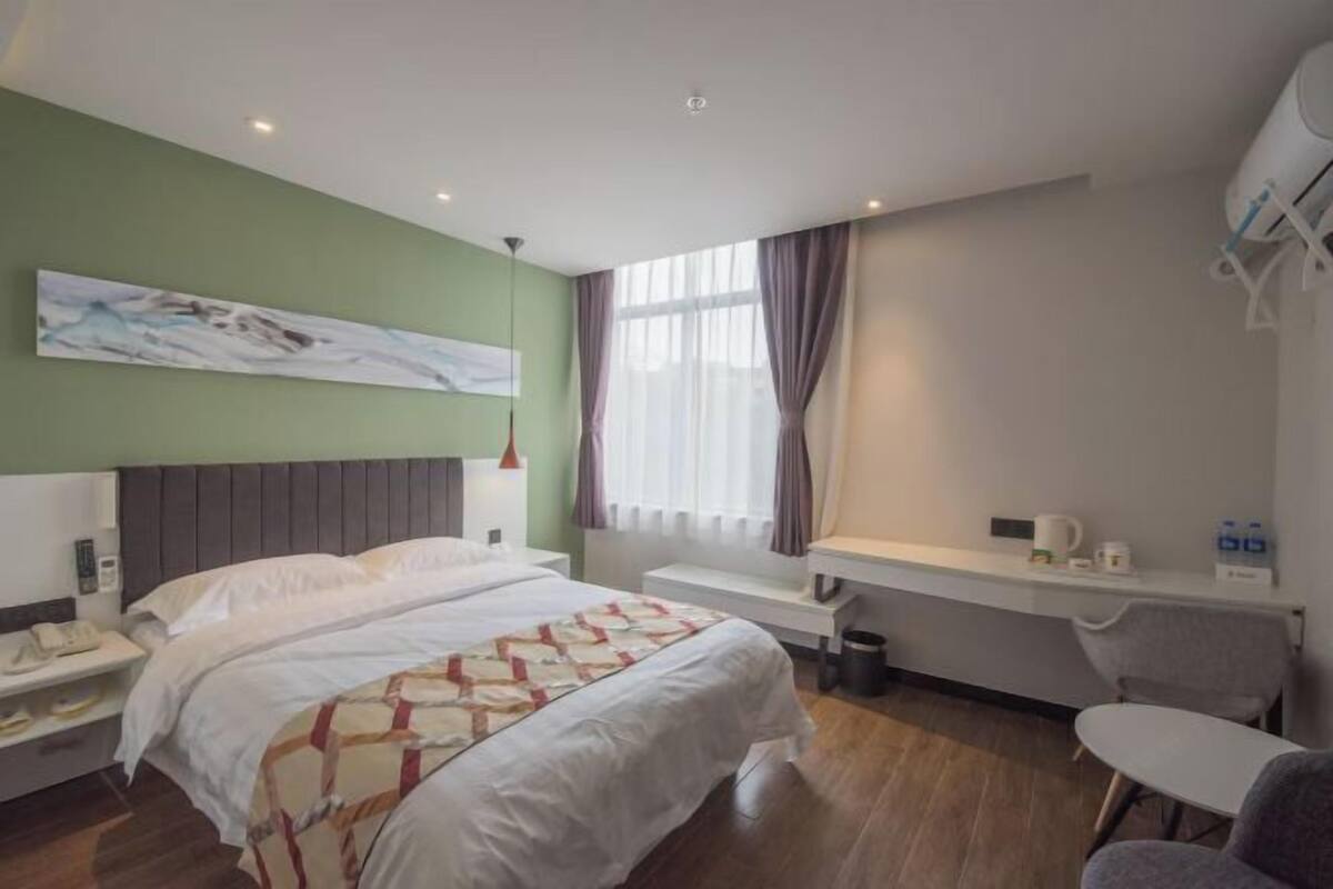 A hotel room with a bed, bedside table, desk, chair, and a window with curtains.