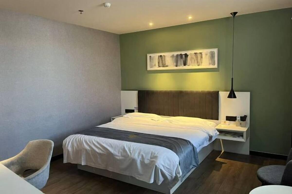 A modern hotel room with a large bed, a bedside table, a chair, and a wall-mounted artwork.