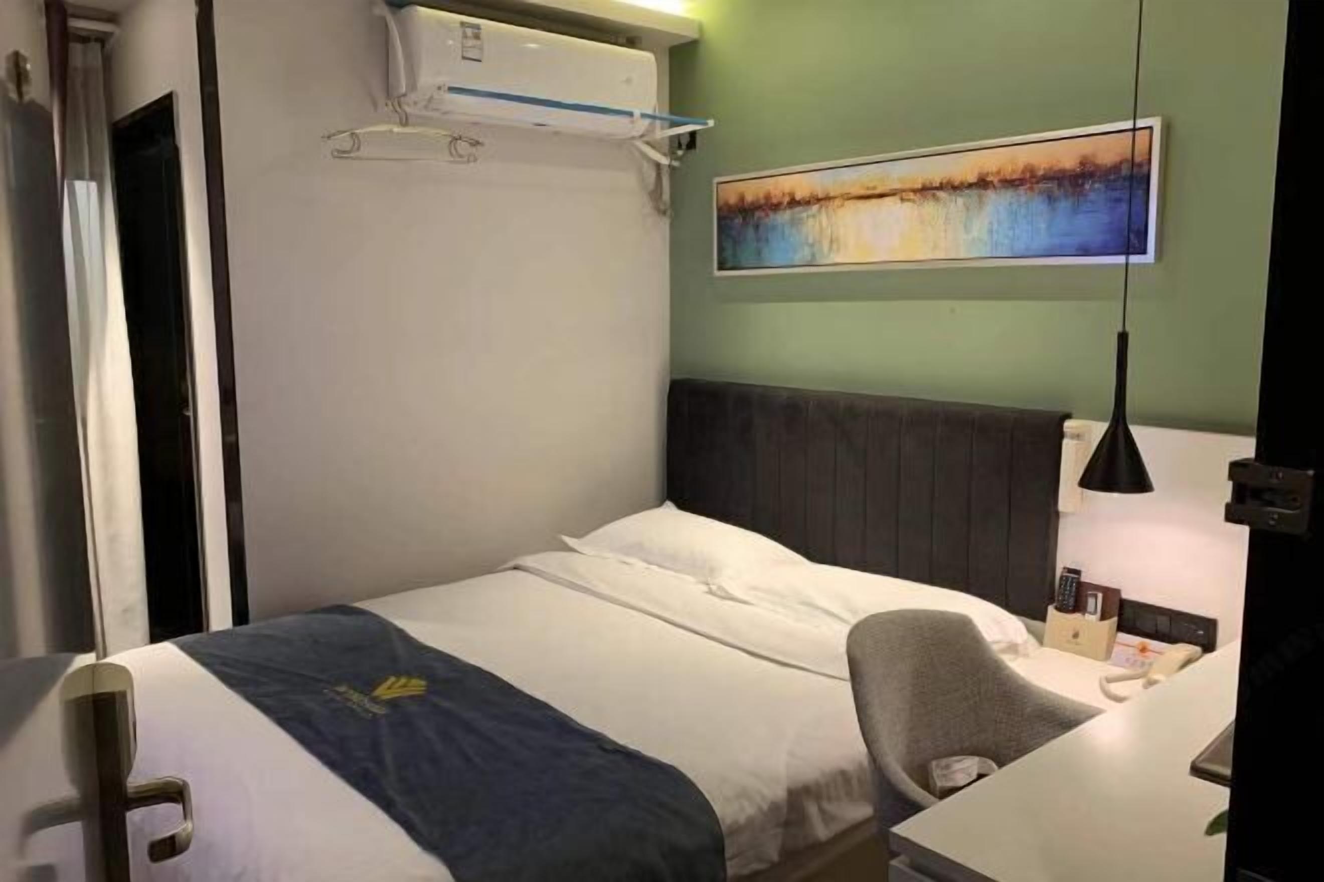 Habitación de hotel con cama, escritorio, silla, un cuadro en la pared y un equipo de aire acondicionado.