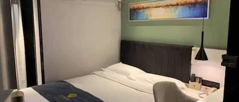 Habitación de hotel con cama, escritorio, silla, un cuadro en la pared y un equipo de aire acondicionado.