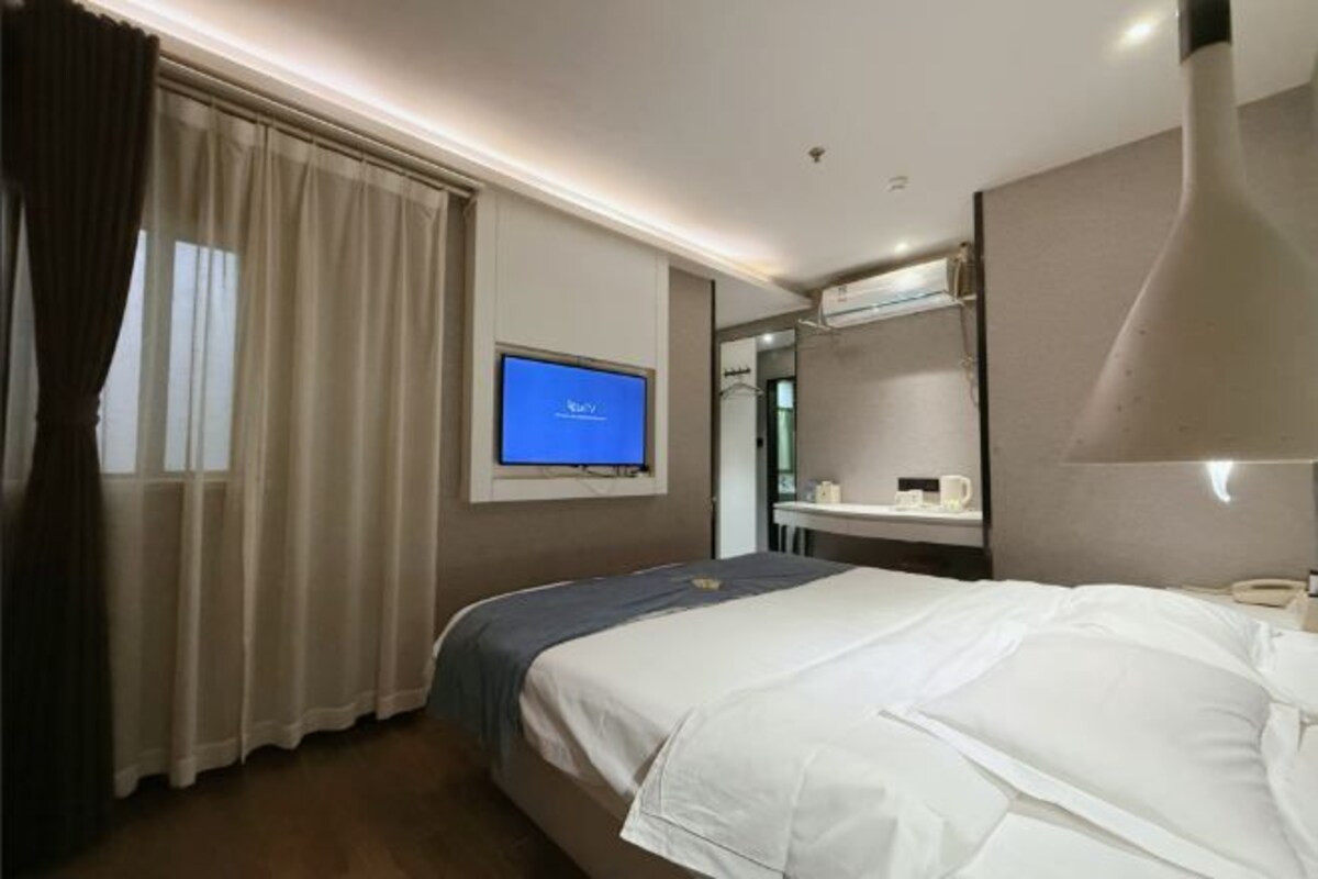A hotel room with a bed, a television, a mirror, and a window with curtains.