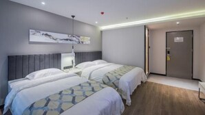 Hotellihuone, jossa on kaksi sänkyä, moderni sängynpääty, taulu seinällä ja lukittava ovi.