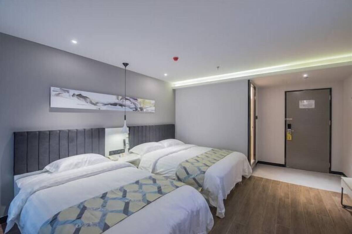 A hotel room with two beds, a modern headboard, a painting on the wall, and a door with a lock.