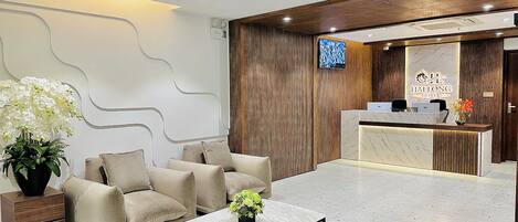 A hotel reception area with a modern design, featuring a reception desk, seating area with sofas, and a decorative plant.