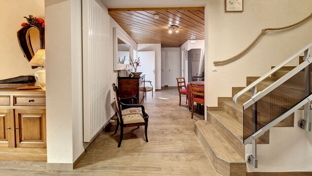 Ein geräumiger Flur mit Holzboden, ein Essbereich mit Tisch und Stühlen sowie eine Treppe mit Glastrennwand.