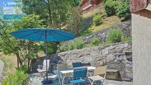 Eine Terrasse im Freien mit Steinboden, einem Tisch, Stühlen und einem blauen Sonnenschirm.