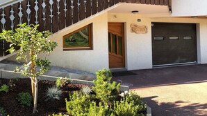Ein modernes, zweistöckiges Haus mit einer Holztreppe, einer Garage und einem kleinen Garten mit verschiedenen Pflanzen.