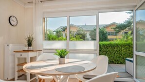 A modern dining area with a round table, white chairs, and a potted plant. - Küstenliebe - Moderne und Gemütliche Wohnung mit Weitläufiger Terrasse (Koserow)