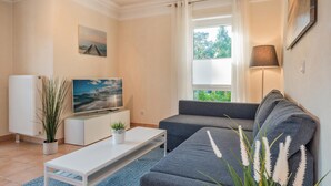 A modern living room with a sofa, TV, and a potted plant. - Küstenliebe - Moderne und Gemütliche Wohnung mit Weitläufiger Terrasse (Koserow)