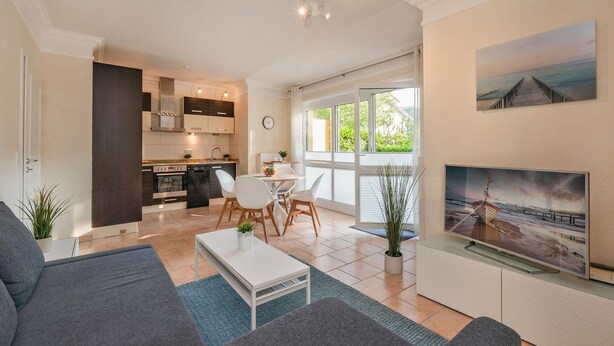 A modern living room with a sofa, coffee table, and TV. There is a kitchen in the background with a dining area. - Küstenliebe - Moderne und Gemütliche Wohnung mit Weitläufiger Terrasse (Koserow)