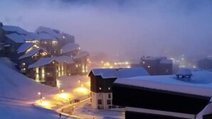 A snow-covered mountain town at dusk with illuminated buildings and a clear view of the mountains in the background.