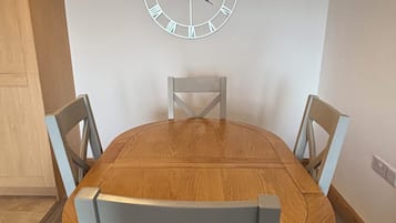 A dining area with a wooden oval table, four light blue chairs, and a wall-mounted clock.