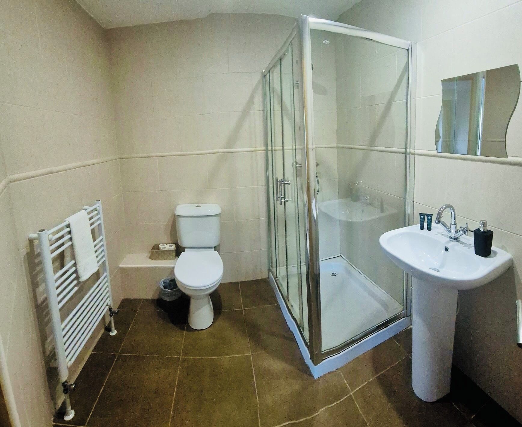 A bathroom with a glass shower enclosure, a white toilet, a white sink, and a towel rack.