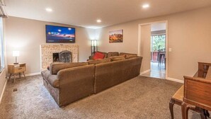 A living room with a sectional sofa, a fireplace, a television, and a door leading to another room.