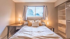 A bedroom with a bed, bedside tables, a window with curtains, and a wardrobe.