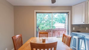 A dining area with a wooden table and chairs, a kitchen with white cabinets, and a sliding glass door leading to a backyard.