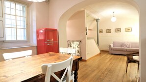 A dining area with a wooden table and chairs, a red refrigerator, and a living room with a sofa and wall-mounted pictures. - Wine Apartments Florence Nebbiolo (Firenze)