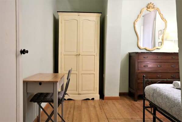 A bedroom with a wooden floor, a bed with a patterned blanket, a wooden dresser, a mirror with an ornate frame, and a wardrobe.