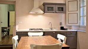 A kitchen with a wooden table, white chairs, a gas stove, and a window with blinds. - Wine Apartments Florence Nebbiolo (Firenze)
