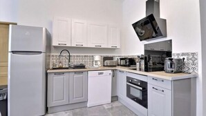 A modern kitchen with white cabinets, a built-in microwave, a coffee maker, and a dishwasher. - Les Appartements Fénelon (Le Cateau-Cambresis)
