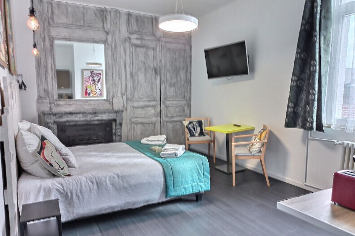 A modern bedroom with a bed, a small table, two chairs, a TV, and a fireplace.