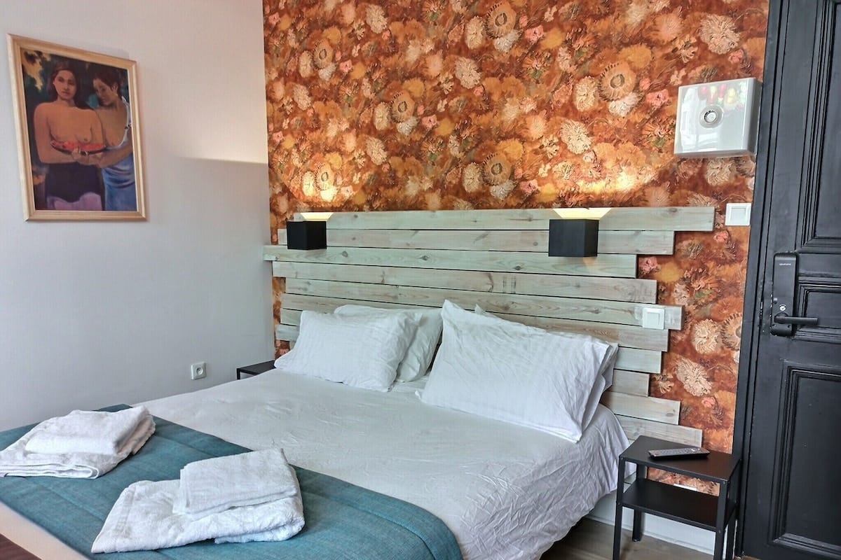 A neatly made bed with white linens and a teal bedspread, a wooden headboard, and a floral-patterned accent wall.