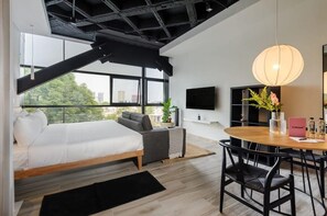 A modern bedroom with a bed, a sofa, a dining table with chairs, a TV, and a large window with a city view. - w* | Well-appointed Loft near Polanco (Ciudad de México)