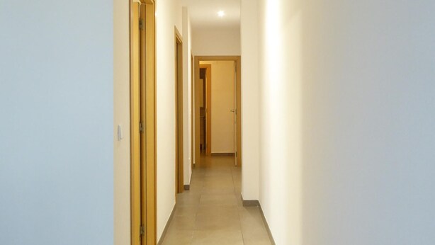 Een smalle, goed verlichte gang met houten deuren en een betegelde vloer, die naar een kamer leidt.