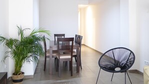 Een eethoek met een tafel, stoelen, een plant in pot en een zwarte stoel.