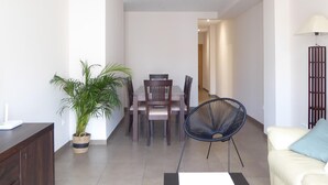 Een moderne woonkamer met eethoek, met een potplant, een bank, een lamp en een eettafel met stoelen.
