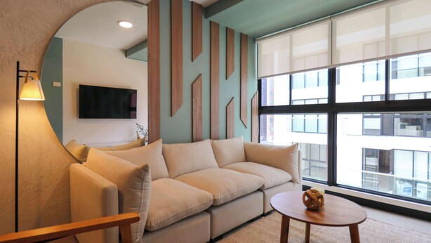 A modern living room with a beige sofa, a round coffee table, and a large window offering a view of buildings. - w* | Captivating 1BR in San Isidro (San Isidro)