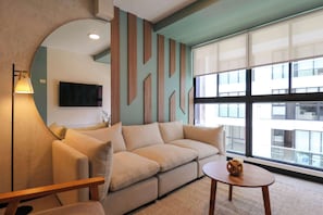 A modern living room with a beige sofa, a round coffee table, and a large window offering a view of buildings. - w* | Captivating 1BR in San Isidro (San Isidro)