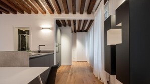 Eine moderne Küche mit Holzbalken, ein Essbereich mit weißem Tisch und ein Flur mit Spiegel und Vorhängen.